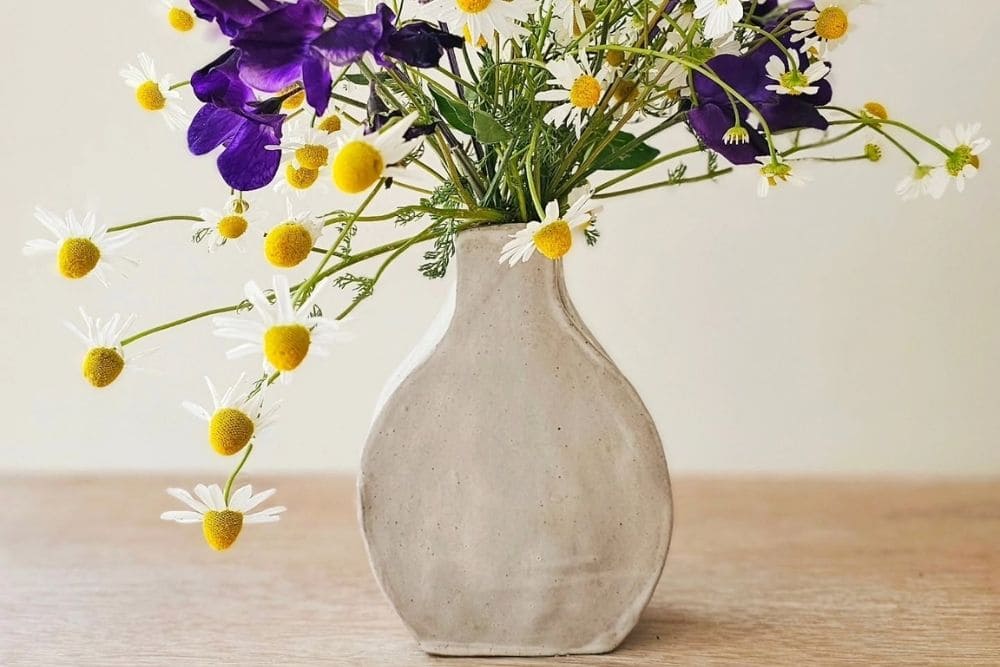 Light grey handmade ceramic vase filled with purple sweet peas and daisies